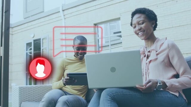 Two women sitting on woven sofa chat bubble appearing, adjusting laptop sharing tablet for business