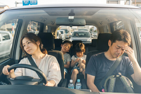 高速道路の渋滞に巻き込まれ、車内で疲れ果てた表情の日本人家族。ドライブ、旅行、ストレス、交通渋滞