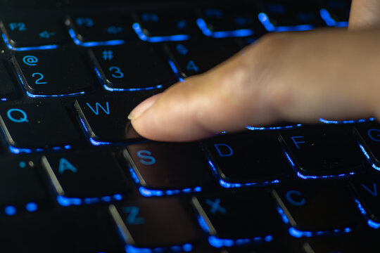 Close up of a finger pressing the W key on a computer keyboard with vibrant blue LED backlight, representing gaming and digital work