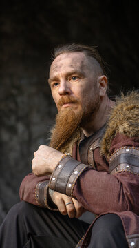 A rugged, bearded man with a weathered face and Viking-inspired attire stares intently into the distance.