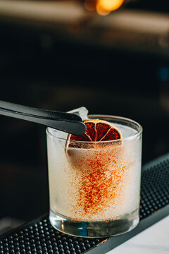 Craft cocktail served in a clear glass with a dried lime slice on a bar counter. A bartender prepares a craft cocktail with a slice of dried lime and spice.
