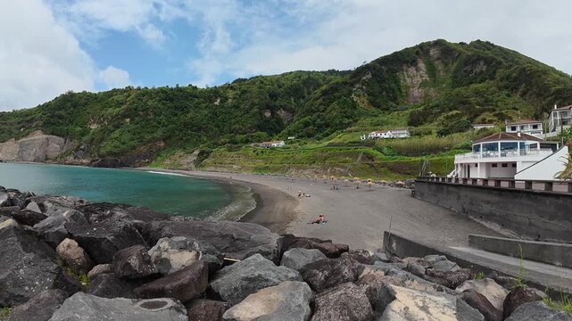 View of green cliffs from a black boulder beach under a cloudy sky