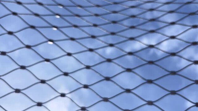 Blue sky and clouds timelapse through metal wire mesh fence with bokeh full frame loop background footage