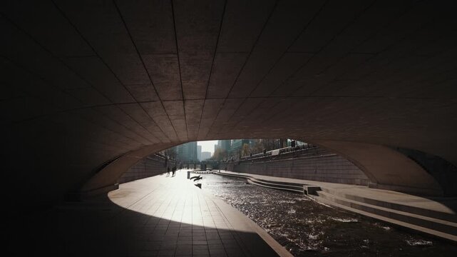 Moody view of Cheonggyecheon Stream under urban bridges with soft light reflections on water surface. Calm and cinematic atmosphere in Seoul city.
