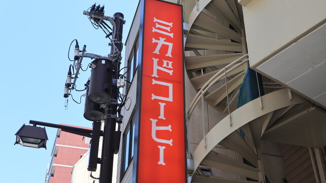 Mikado Coffee vertical shop sign in red and white next to a modern metal spiral staircase and utility pole with transformers under a clear blue sky - Tokyo, Japan, May 15, 2024