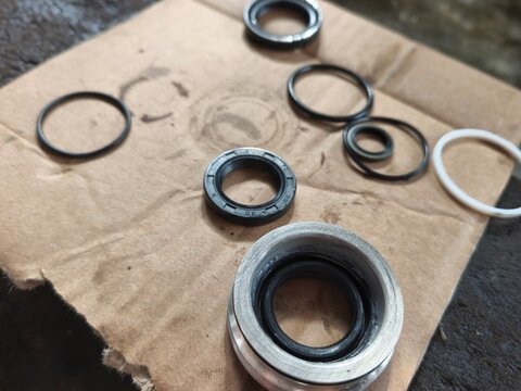 A close-up shot of various automotive seals, O-rings, and gaskets arranged on a piece of cardboard in a workshop. The rubber and metal components appear clean, highlighting the parts needed for engine