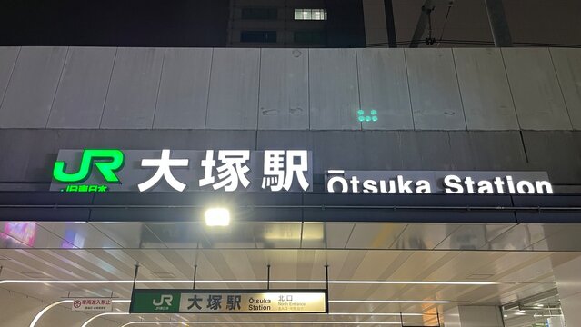 JR Otsuka Station north entrance illuminated signage at night featuring the green East Japan Railway Company logo and English romanization - Tokyo, Japan, November 12, 2024