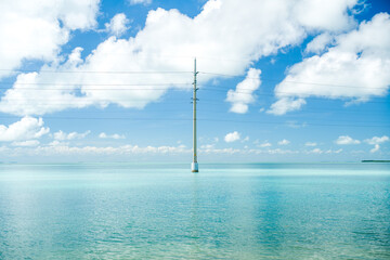 Obraz premium Electric power pole standing in the shallow sea water under the cloudy sky near the Florida Keys horizon on a bright day.