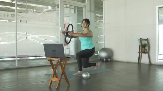 Woman following online pilates class with magic circle