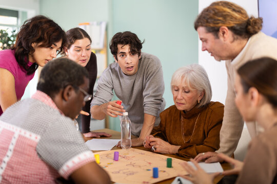 Engaged men and women of different ages playing tabletop game during interactive workshop indoors
