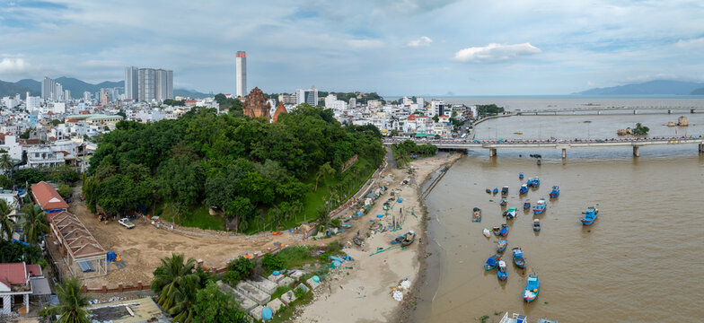 Nha Trang, Vietnam - A panoramic view of the Cai River with numerous fishing boats docked along the shore and a bridge spanning the water, with the city skyline in the background. Po Nagar Temple,