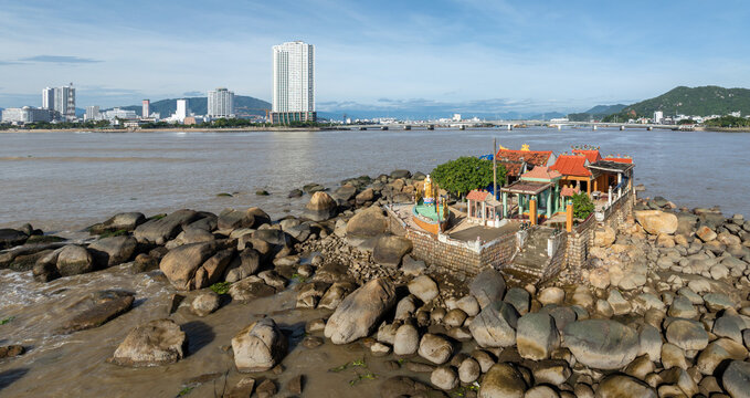 A scenic view of the Nha Trang coastline in Vietnam, featuring Mieu Ong temple on rocky outcrops with the city skyline in the background.
