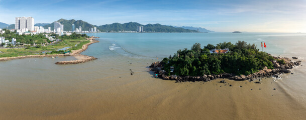 Obraz premium A serene aerial view of Chua Tu Ton temple on a rocky island off the coast of Nha Trang, Vietnam. The Buddhist temple, surrounded by lush greenery, overlooks the calm sea.