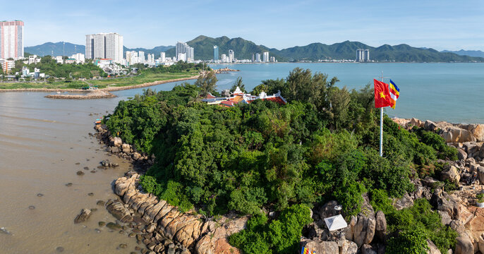 A serene aerial view of Chua Tu Ton temple on a rocky island off the coast of Nha Trang, Vietnam. The Buddhist temple, surrounded by lush greenery, overlooks the calm sea.