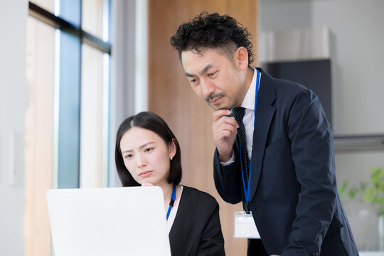 パソコンの前で真剣な表情で考える悩むデスクワーク業務に取り組む上司と部下の男女のビジネスマンチーム　この問題、課題どうしようかな～
