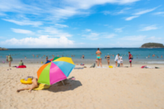 Blurred image of tourists relaxing on the white sand beach under a blue sky on summer vacation