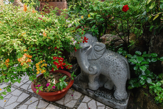 A stone elephant statue adorned with bougainvillea flowers in a garden in Po Nagar Temple, Nha Trang,  Vietnam. The statue is a decorative element in a lush, green outdoor space.