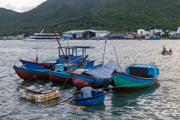 Obraz premium A fisherman in a small boat prepares his nets near colorful fishing vessels in Nha Trang, Vietnam. The scene captures the daily life of local fishermen.