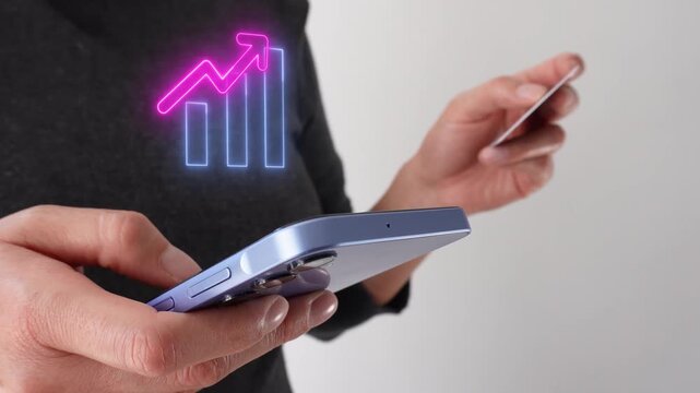Positive trend. Businesswoman holding a bank card while holding a smartphone with a virtual bar graph icon with an upward-pointing arrow.