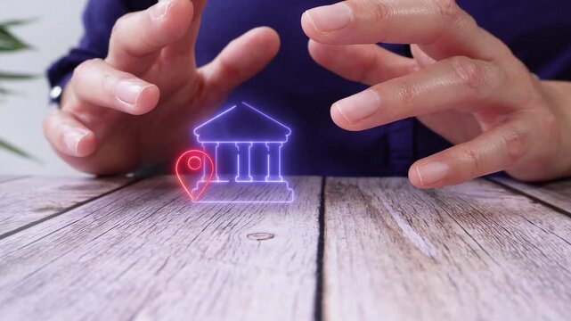 Location of bank branches. Close-up of a pair of hands on a table, protecting a virtual bank icon with a location pin.