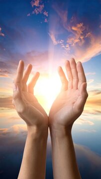 Hands cupped towards brilliant sunlight bursting through a vibrant, colorful sky