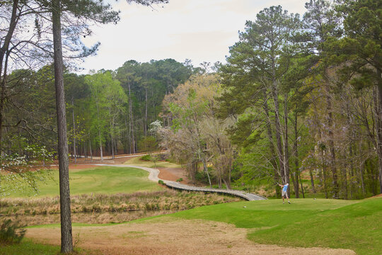Golfer teeing off at a scenic golf course with a rustic wooden bridge