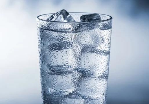 A refreshing glass of sparkling water filled with clear ice cubes against a soft purple background