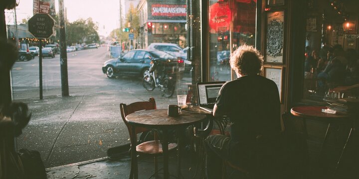 urban coffee shop worker using laptop by window overlooking city street traffic