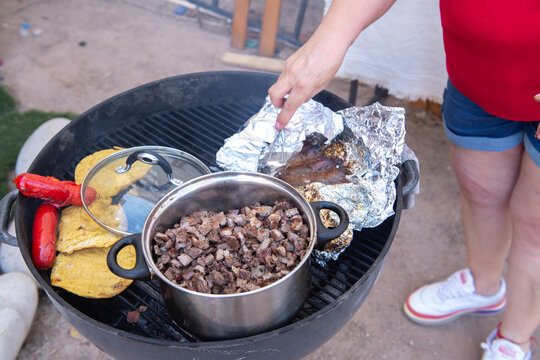Comida en reunion familiar en el patio trasero de una casa Mexicana, con carne asada, tortillas de Maiz y harina para hacer tacos en una parrilla al carbon, tortillas y chorizo, olla con carne de res.
