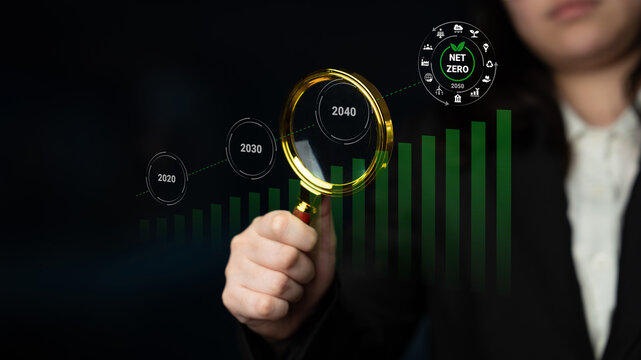 A business professional analyzes growth projections using a magnifying glass, highlighting net zero goals for future sustainability. Focus on impact and responsibility. Gantry