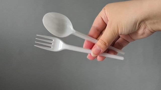Plastic spoon and fork in hand on a gray background. set disposable takeaway tableware