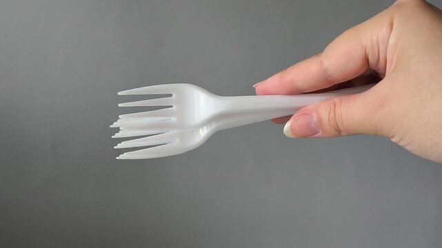 A set of disposable plastic forks in hand on a gray background. Set of dishes