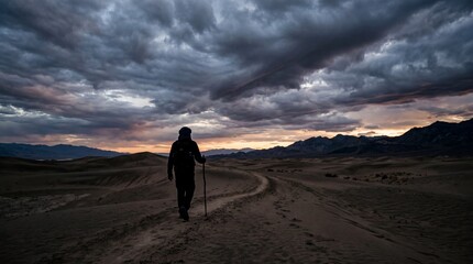 Obraz premium Silhouette of a traveler walking through a desert landscape under a dramatic cloudy sky at dusk
