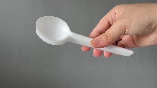 A set of white plastic spoons in hand on a gray background. Tableware set