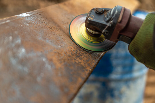 Deleting rust. Close photo grinding of a rusty metal angle with a grinding disc and grinder. Work in green gloves on the street. High quality photo