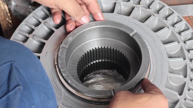 Close up of a technician's hands carefully fitting a rubber piston seal ring into a metal transmission part during a gearbox overhaul.