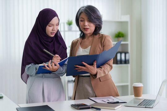 Asian businesswomen colleagues reviewing documents folder together discussing business project report teamwork collaboration modern bright office workplace
