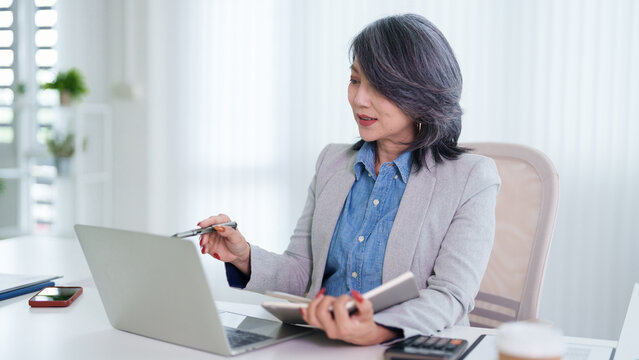 Asian business woman senior professional working laptop computer calculator notebook financial report analysis office desk modern workplace planning budget