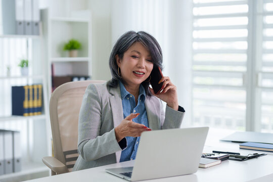 Asian businesswoman talking phone using laptop computer working from modern office desk professional consultant manager discussion client video conference call