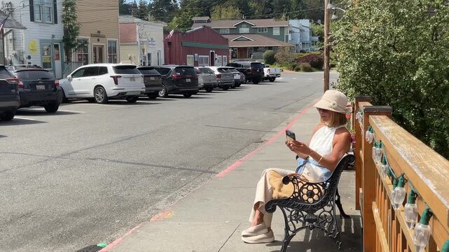 Woman sitting on a bench in a small town taking a selfie picture on her phone. 