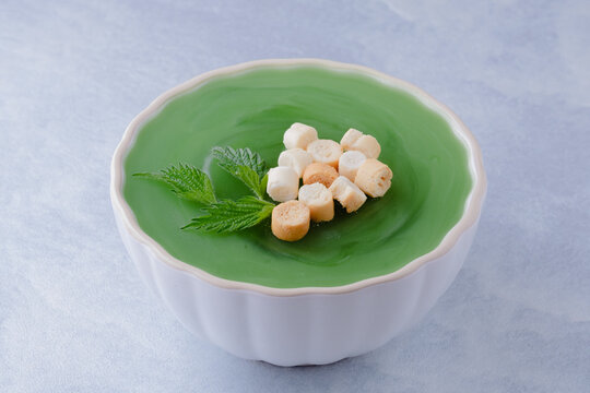 Vibrant green and luxuriously smooth, this nettle soup is a fresh and foraged spring delicacy on a blue background. Topped with small pieces of bread. Healthy detox food
