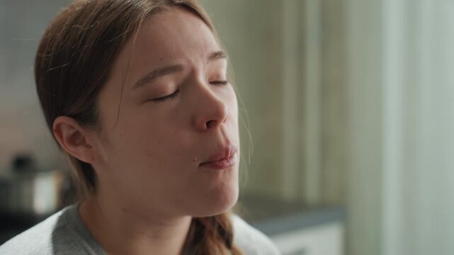 Pregnant woman experiencing intense nausea, closeup. Teary eyes and sweating forehead, slow breathing to ease discomfort, muted morning light in domestic kitchen, intimate vulnerable portrait showing