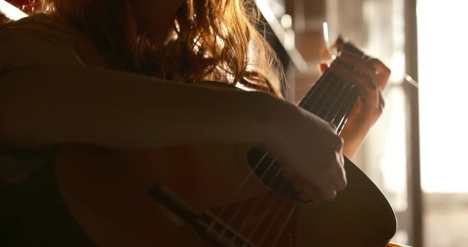 A cinematic close up a teenage girl with red hair playing a classical guitar in a cozy home interior during sunset. Warm golden light streams through a nearby window, softly