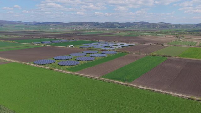 Unique circular solar panel arrays surrounded by green and plowed agricultural fields under a beautiful spring sky, medium altitude forward drone flight, 4K