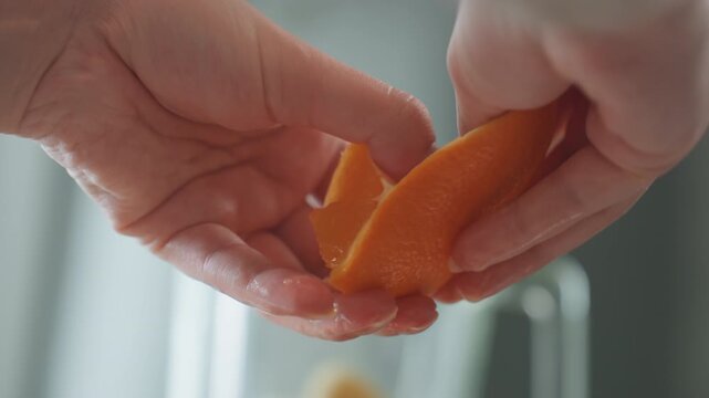 Closeup hands passing orange segment across countertop, tender offering in soft daylight, moist citrus pulp and bright zest, quiet hospitality moment suggesting care and nourishment, calm domestic
