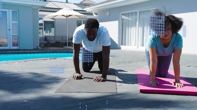 After positioning hands on mats, woman and man moving into plank at poolside for fitness demo