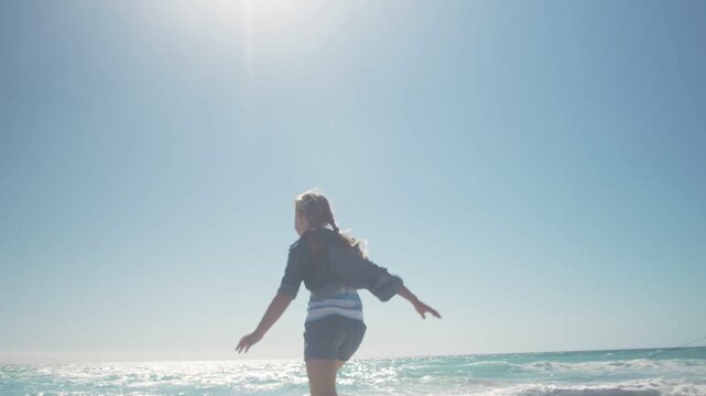 Female adult entering frame, running and jumping over rope toward waves, promoting travel marketing