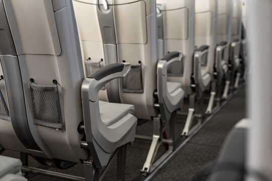 Modern airplane cabin interior with ergonomic grey economy class seats, foldable tray tables, mesh storage pockets and metal supports, soft ambient lighting, clean minimal design.