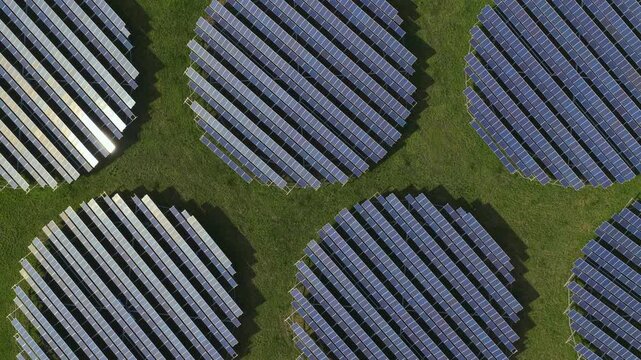 Dynamic sun reflections on detailed circular solar panel arrays, low altitude top down slow lateral drone shot, 4K