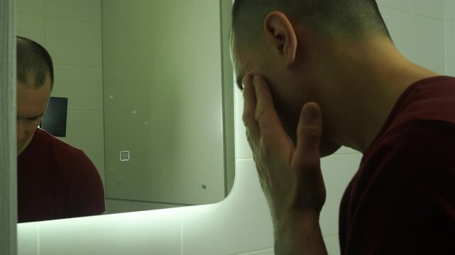 Morning routine. A man washes his face in front of a mirror.